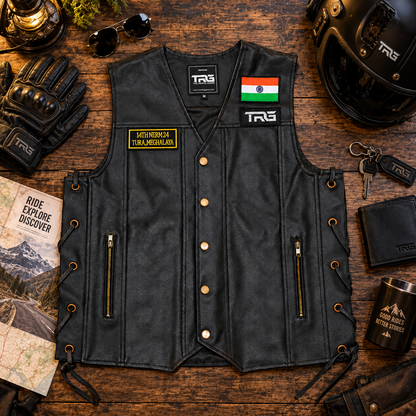 Flat lay of black motorcycle riding vest with Tura Meghalaya NERM patch surrounded by helmet, gloves, keys and riding accessories