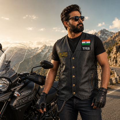Rider wearing 90,000 Kilometres embroidered patch on black leather vest beside adventure motorcycle in mountain setting